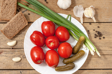Fermented food on a white plate on an old wooden table. Pickled tomatoes and cucumbers. Salt for the winter. Traditional snack for alcohol.