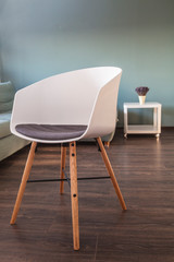 Modern scandinavian chair, made of wood and plastic with fabric seat in living environment, with parquet and green wall in background, interior design concept
