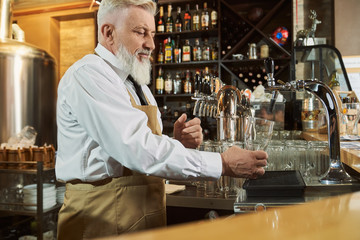 Barman standing at bar counter pouring beer in glass.