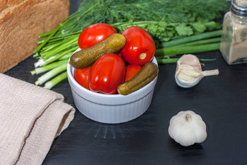 Fermented food on a white plate on an black wooden table. Pickled tomatoes and cucumbers. Salt for the winter. Traditional snack for alcohol.