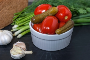 Fermented food on a white plate on an black wooden table. Pickled tomatoes and cucumbers. Salt for the winter. Traditional snack for alcohol.
