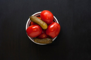 Fermented food on a white plate on an black wooden table. Pickled tomatoes and cucumbers. Salt for the winter. Traditional snack for alcohol.