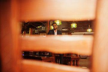 Handsome well-dressed arabian man with glass of whiskey and cigar posed at pub.
