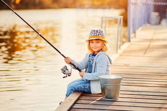 A little girl fishing with a fishing rod from a pontoon or pier on the pond  fish farm Stock Photo