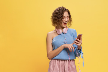 Model with pink headphones holding phone, smiling.