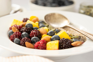 Healthy breakfast with oatmeal porridge, fruits and nuts. Blueberry, mango, pumpkin seeds, nuts, coffee cup. Top view white background. Clean eating, dieting, weight loss concept
