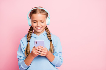 Photo of pretty little lady holding telephone hands turning on new popular youth song in earflaps wear casual blue hoodie pullover isolated pastel pink color background