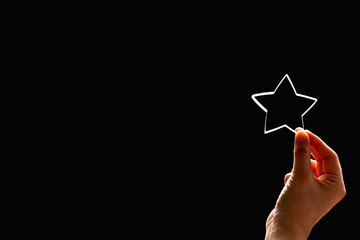 A woman gives a star. The concept of a positive rating, reviews and feedback on black background.