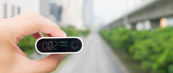 Closeup hand holding air quality monitor to detect level of pollution or small particulate (PM 2.5) in the city and it's show very low with green light, which mean air quality is good and safe. AQI.