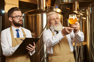 Brewers looking at beer glass, analyzing, writing.