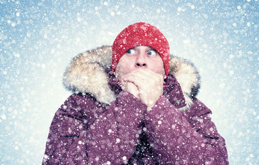Frozen man in red winter clothes warms his hands, cold, snow, frost, blizzard 