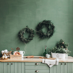 Christmas / New Year composition. Festive christmas decorations on the kitchen with handmade wreath made of fir branches, gold and white toys. Winter holidays concept.