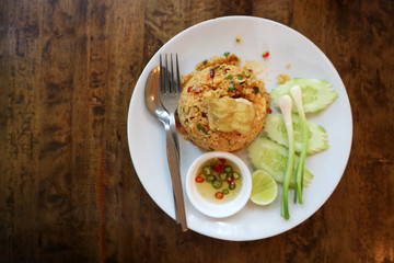 Top View Seafood Tom Yum Fried Rice Served in a white round dish With fish sauce, peppers, cucumbers and spring onions on a wooden table