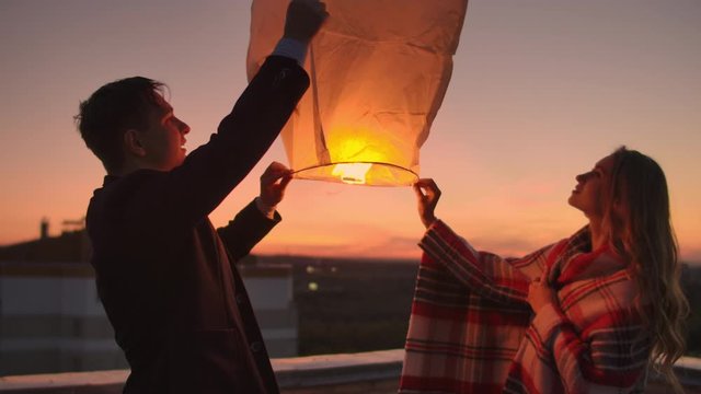 A man and a girl in a plaid launch a sky lantern on the roof