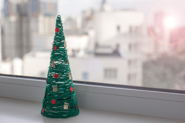 Artificial tree in the shape of a cone stands on a windowsill. Christmas tree made of threads. Handmade decoration. Christmas decor. Postcard. Place for text