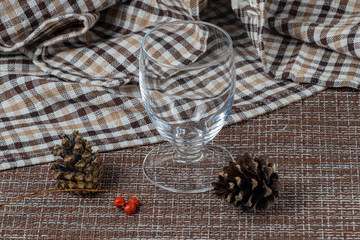 Empty transparent glass on a checkered white and brown kitchen towel. Spruce cones and red berries on a foreground. After the Christmas party.