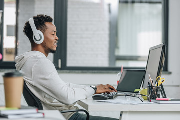 smiling african american programmer in headphones sitting at workplace in office