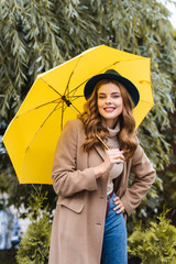 attractive woman in blue hat looking at camera and holding yellow umbrella