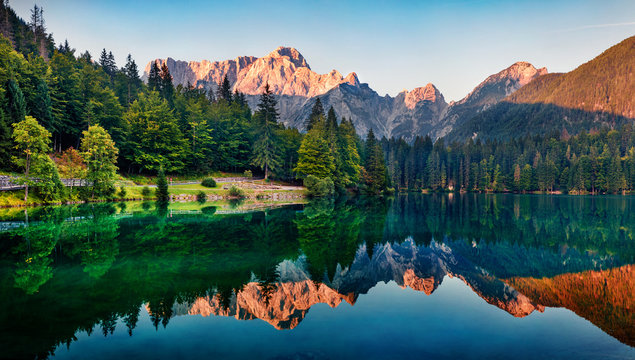 Calm morning view of Fusine lake. Colorful summer sunrise in Julian Alps with Mangart peak on background, Province of Udine, Italy, Europe. Beauty of nature concept background.