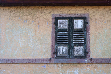 Ein morscher und maroder Fensterladen eines Fensters an einer ausgebleichten Fassade...
