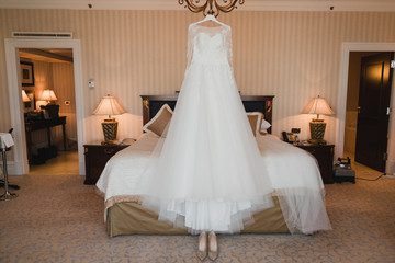 Modern bridal fashion. White wedding dress hanging in the hotel room.