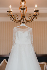 Modern bridal fashion. White wedding dress hanging in the hotel room.