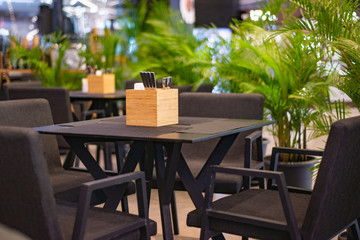 cafe with brown tables and chairs, tableware on the tables in the supplies, around the green indoor palm trees