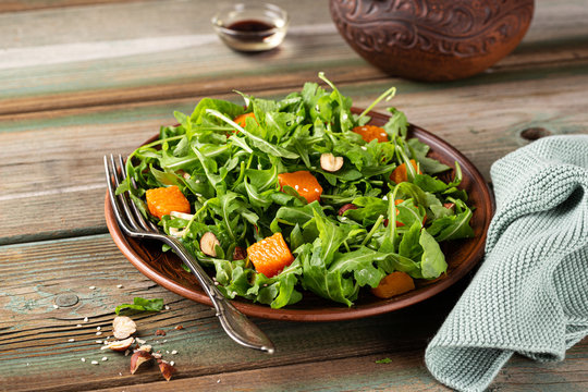 Delicious salad with arugula, baked pumpkin, hazelnut and sesame seeds on brown plate. Paleo diet food concept with copy space.