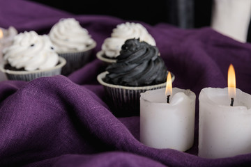 selective focus of tasty Halloween cupcakes and burning candles on purple cloth