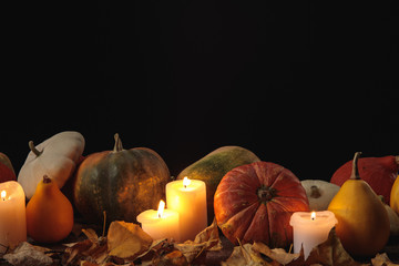 dry foliage, burning candles, ripe pumpkins on wooden rustic table isolated on black