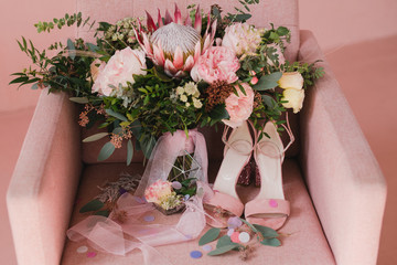 Botanic bridal chic. Bouquet with silk ribbons, female classic shoes, wedding rings and engagement ring on a pink vintage chair.
