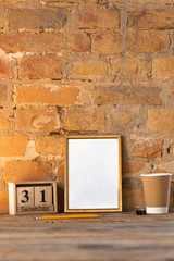 Mock up blank empty picture or sheet on the brown brick wall background with coffee cup and pencils. Copyspace, negative space for your advertising. 31 of December, New Year concept.