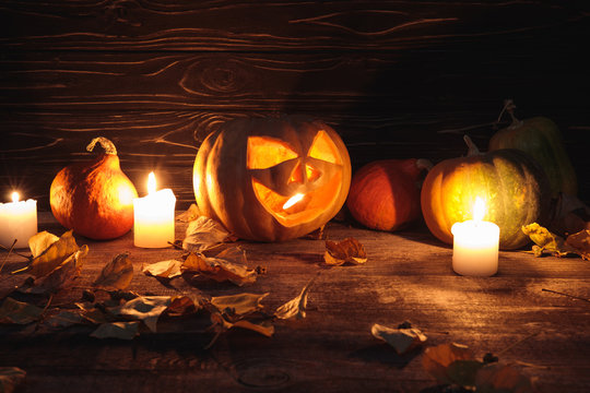 spooky Halloween pumpkin, autumnal leaves and burning candles on wooden rustic table