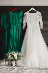 Modern bridal fashion. White wedding dress and green bridesmaids dresses hanging in the hotel room.