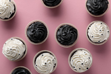 top view of delicious Halloween cupcakes with white and black cream on pink background