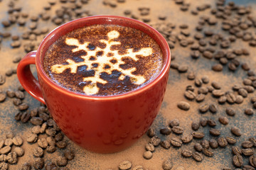 A foamy mug of cappuccino coffee with chocolate snowflake motif and chocolate background with a scattering of coffee beans sets the scene for a festive Christmas and warming up in cold winter weather