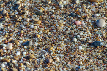 sea pebbles colored granite on the beach background stones. The shore of the beach with sand and pebbles washed by the waves of the sea.