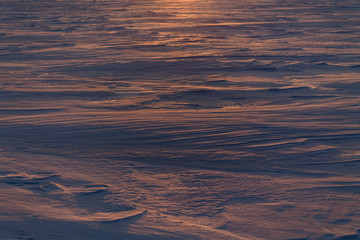 Early morning on a snowy lake. Waves on the snow after the wind. Orange dawn