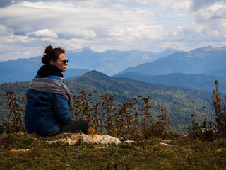 Naklejka premium Girl travels in the mountains. A girl in a denim jacket, sunglasses and a scarf on her head.