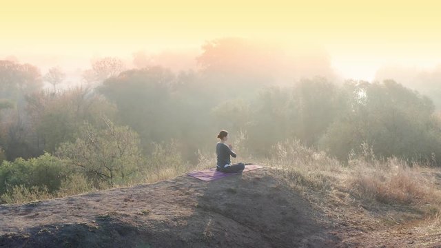 Aerial video. Young woman doing yoga in quiet scenery. Yoga girl practicing pilates on top of the hill. Yoga, sport and healthy lifestyle concept
