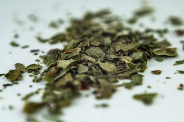 Fototapeta na wymiar green dry crushed leaves (marijuana, tobacco) on a white surface