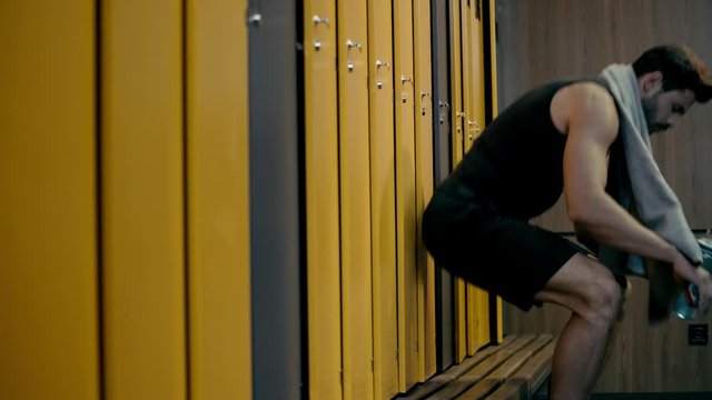 tired man drinking water in locker room 