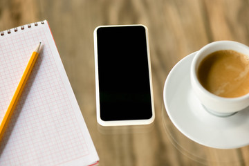 Mock up empty black smartphone screen on wooden table background with pencils, notes and cup of coffee. Copyspace, negative space for your advertising, office and business style.