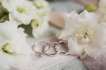 Obraz na płótnie Canvas Modern wedding jewelry. Closeup of two wedding rings and engagement ring on natural background with flowers and leaves.