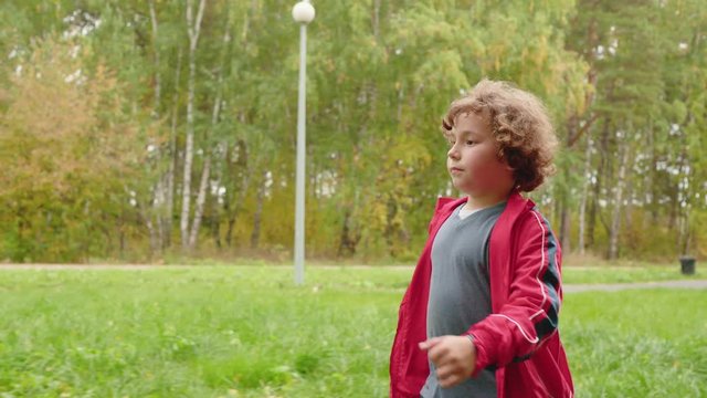 Adorable Preteen Boy Walking through Green Park. Caucasian Teenage Schoolchild Going on Road. Funny Schoolboy with Curly Red Hair. Cute Fatty Kid on Beautiful City Parkland Pathway