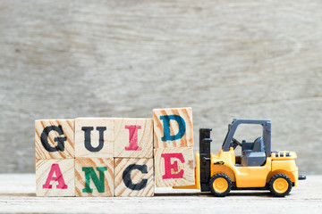 Toy forklift hold letter block d, e to complete word guidance on wood background