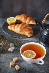Lemon tea, two fresh croissants and teapot