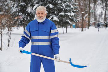 Worker looking at camera while removing snow with shovel