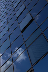 Bottom view of blue glass surface of building wall reflecting blue sky with clouds