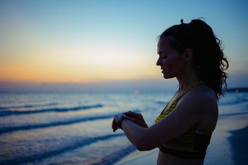 Fototapeta na wymiar healthy sports woman on seacoast in evening using smart watch